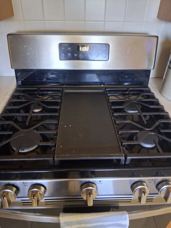 Gas range with crumbs on the center griddle and smudges on the control panel, before a deep cleaning in the Woodland Hills area